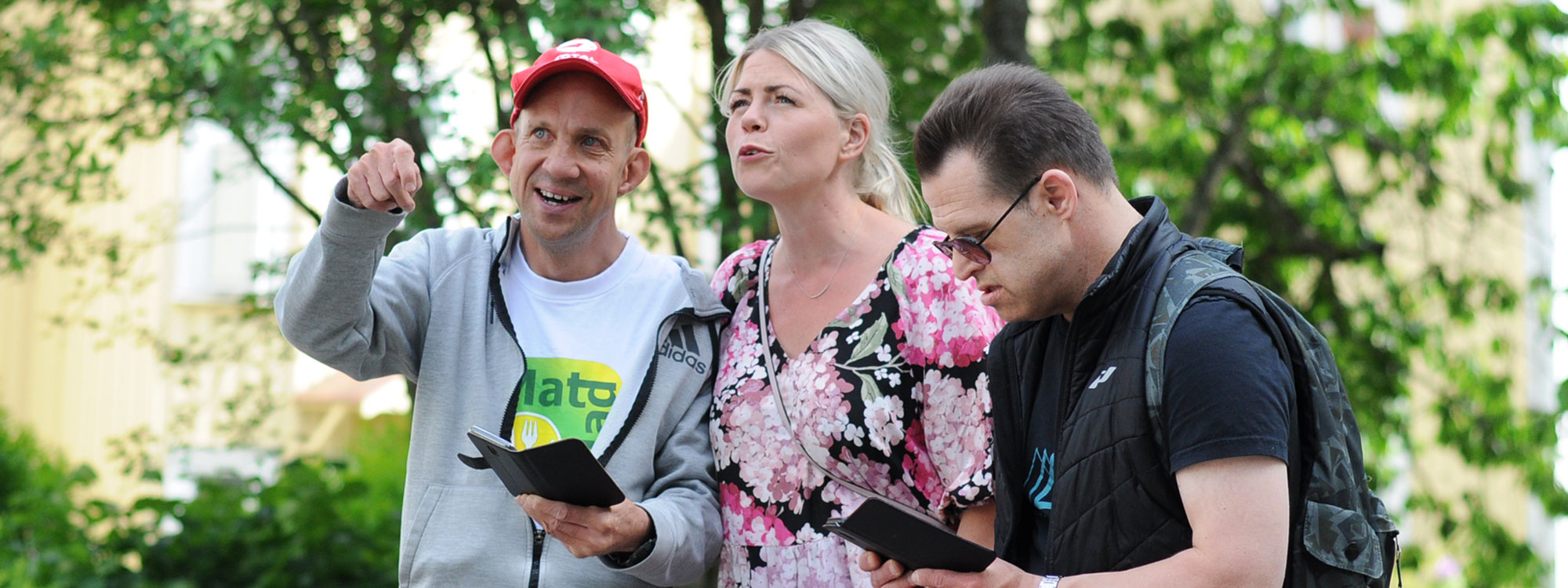 Två män och en kvinna är utomhus. De har smartphones och spelar GoGlad.